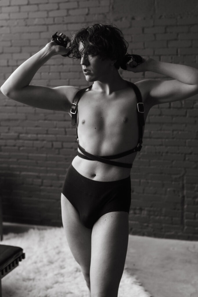 gay man showing his confidence Harrison black and white photo wearing chest harness.